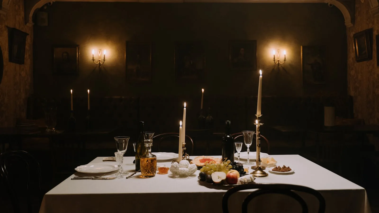 A dimly lit dining room with elegantly set table, decorated with candles, wine, and fruits for a cozy atmosphere.