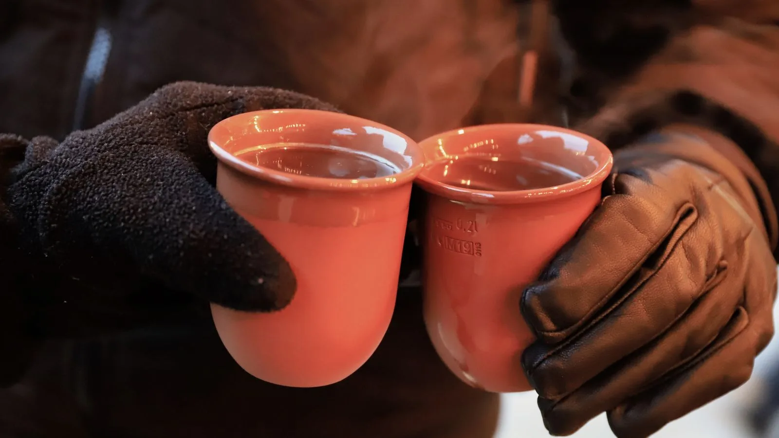 Two hands clink warm mugs of gluhwein at a Kassel Christmas market.