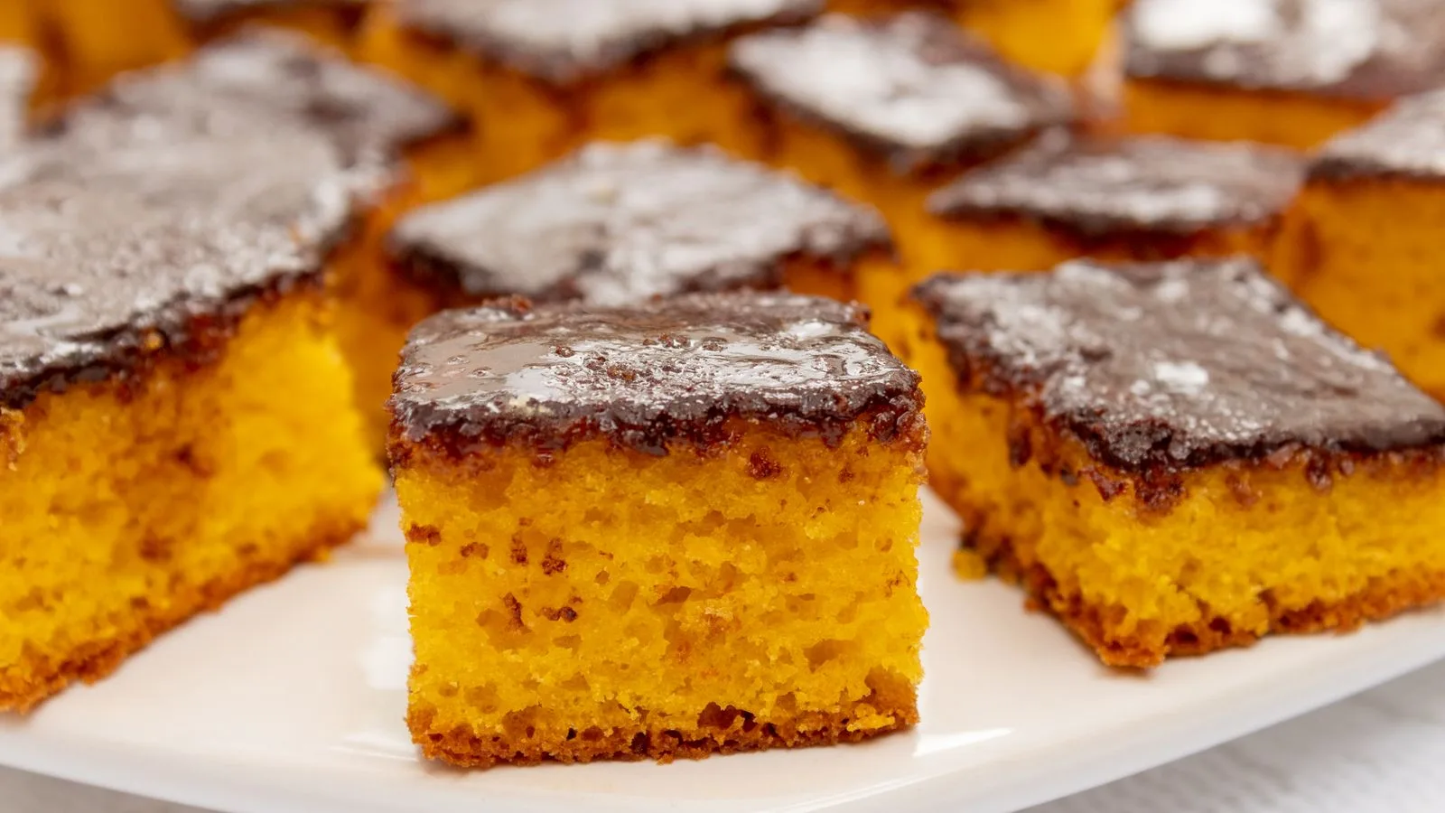 Close-up of moist carrot cake squares with chocolate glaze on a white plate.