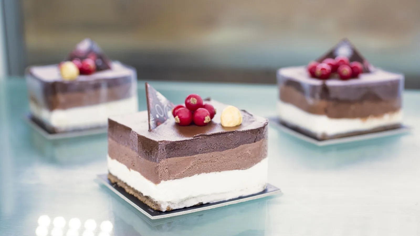 Delicious chocolate mousse cakes with berries and nuts on a glass surface.