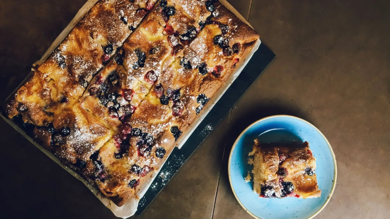 Freshly baked berry cake with icing sugar served on a rustic wooden table.
