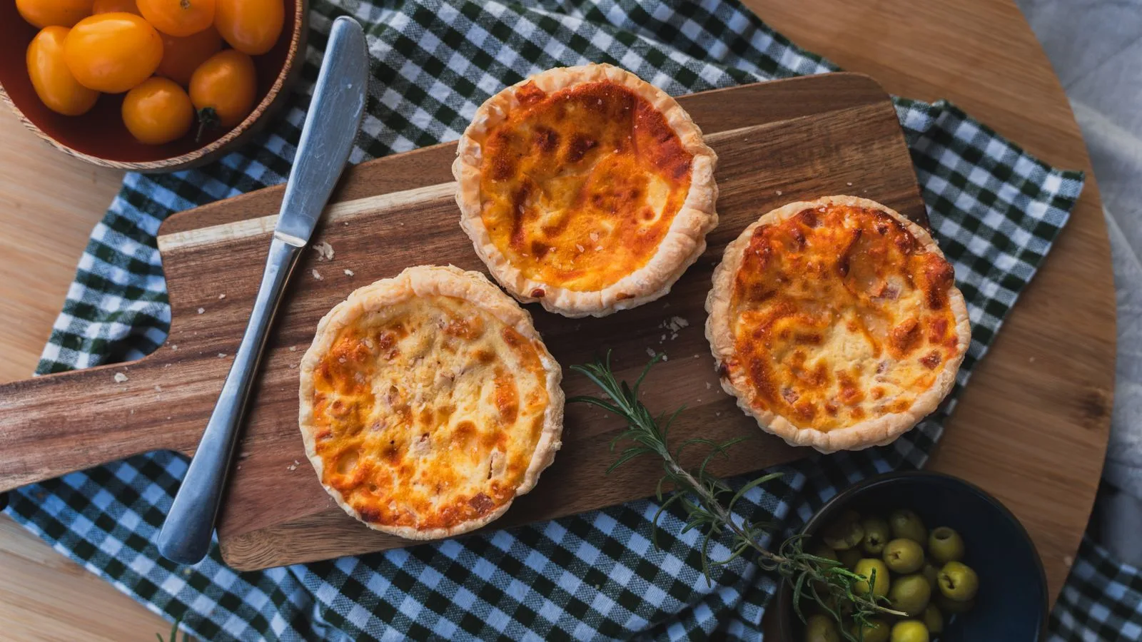 Three freshly baked mini quiches on a cutting board with garnish and colorful ingredients.