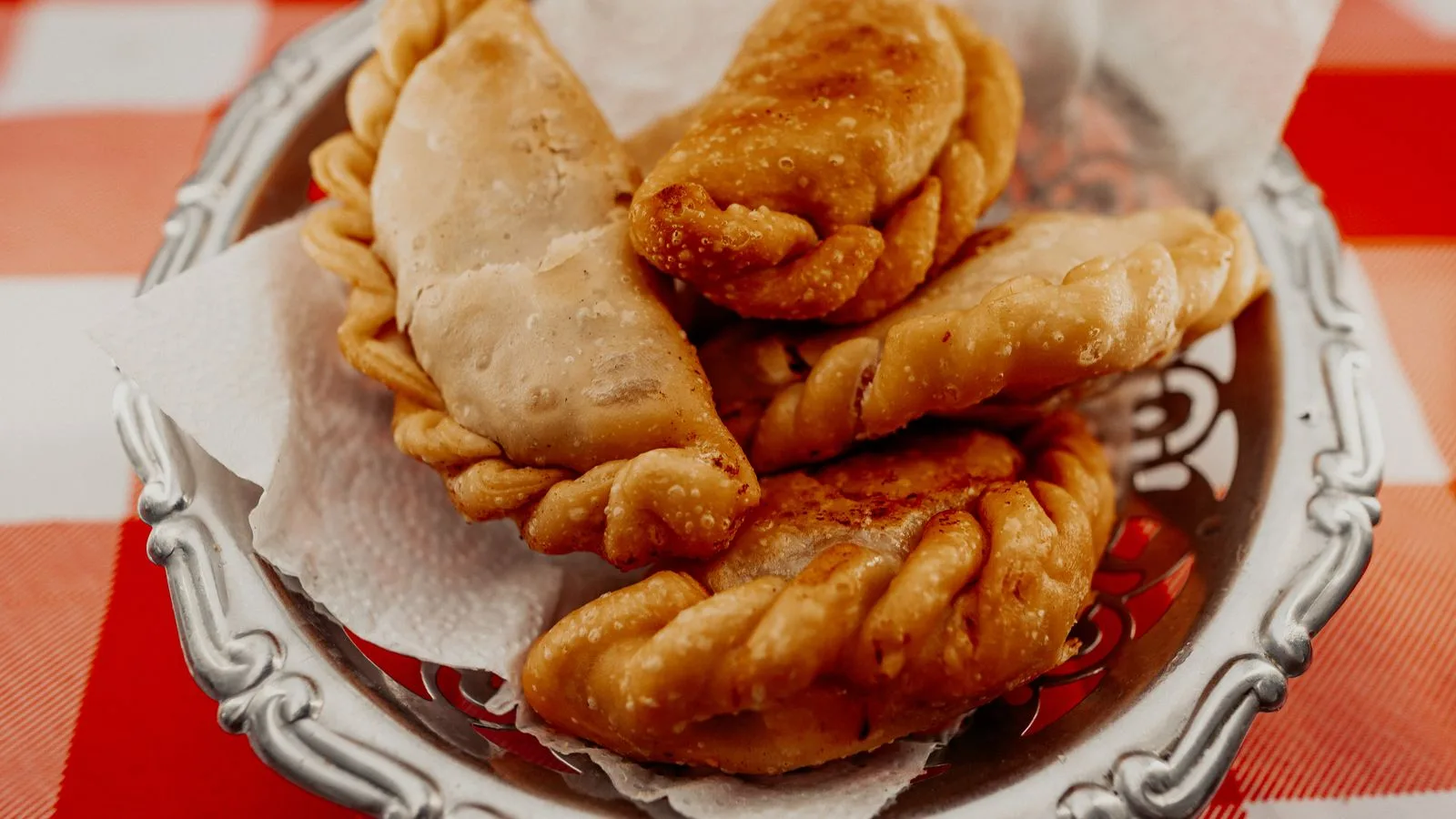 Tasty Argentine empanadas served on a rustic plate with a red checkered tablecloth.