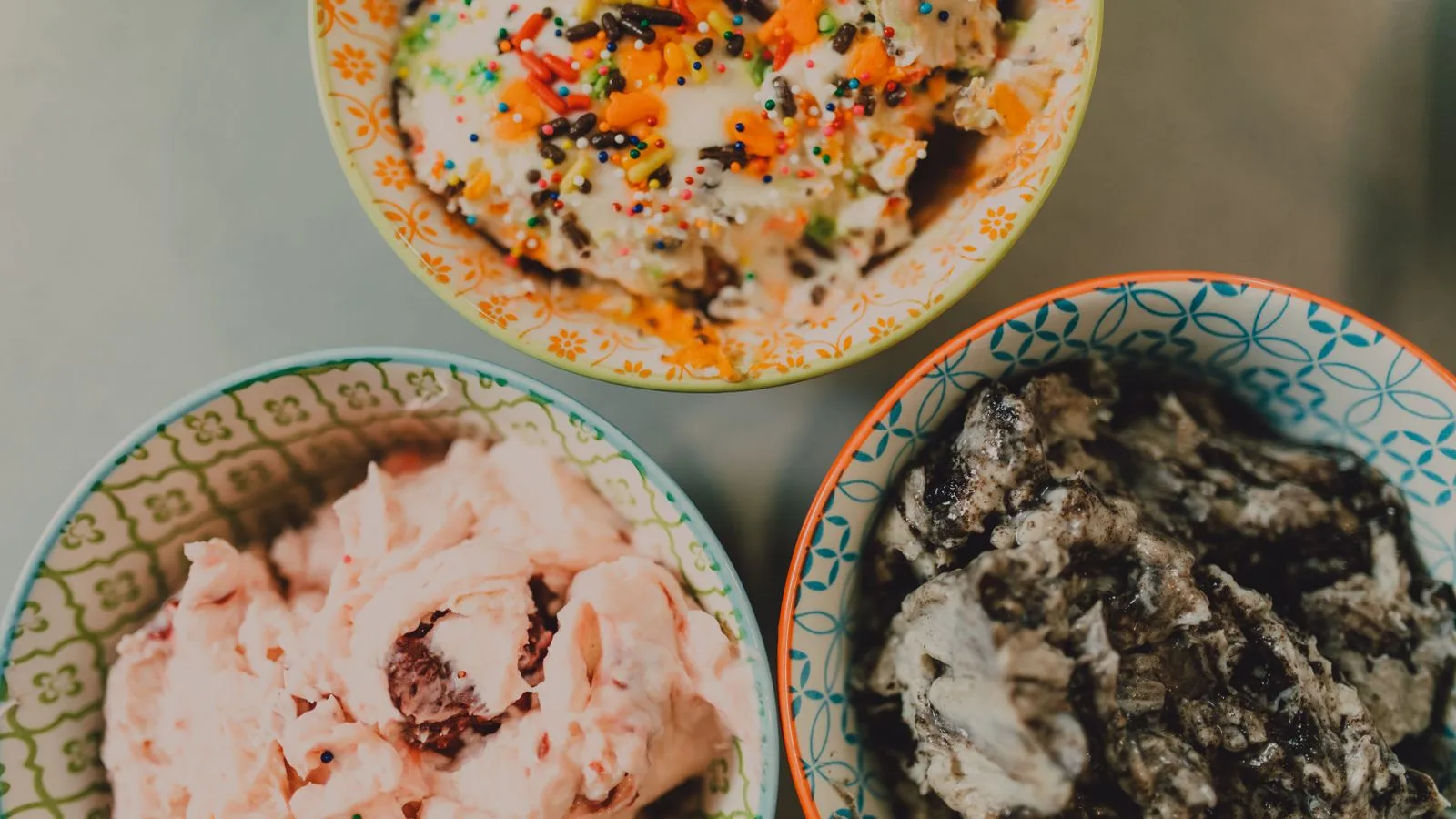 Top view of three colorful bowls filled with various ice cream flavors and toppings.