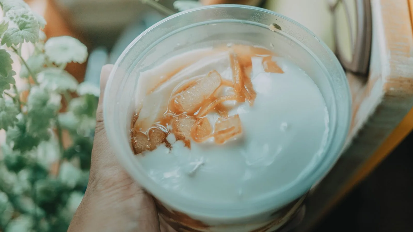 Close-up of a hand holding a cup containing a creamy coconut dessert with sliced toppings.