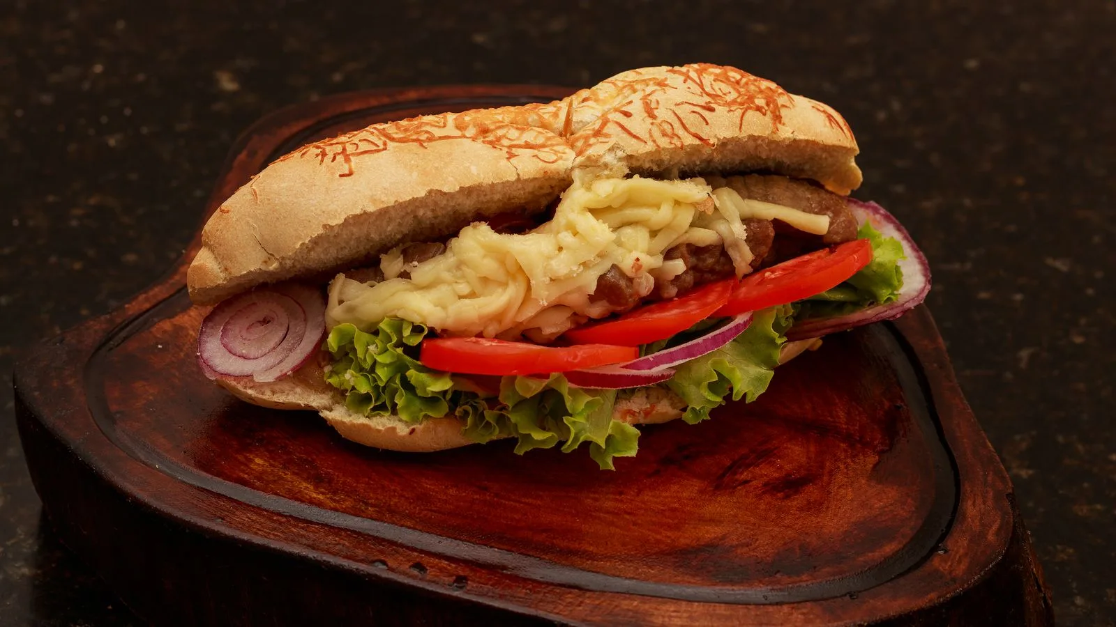 Tasty chicken sandwich topped with lettuce, tomatoes, and cheese on a rustic board.