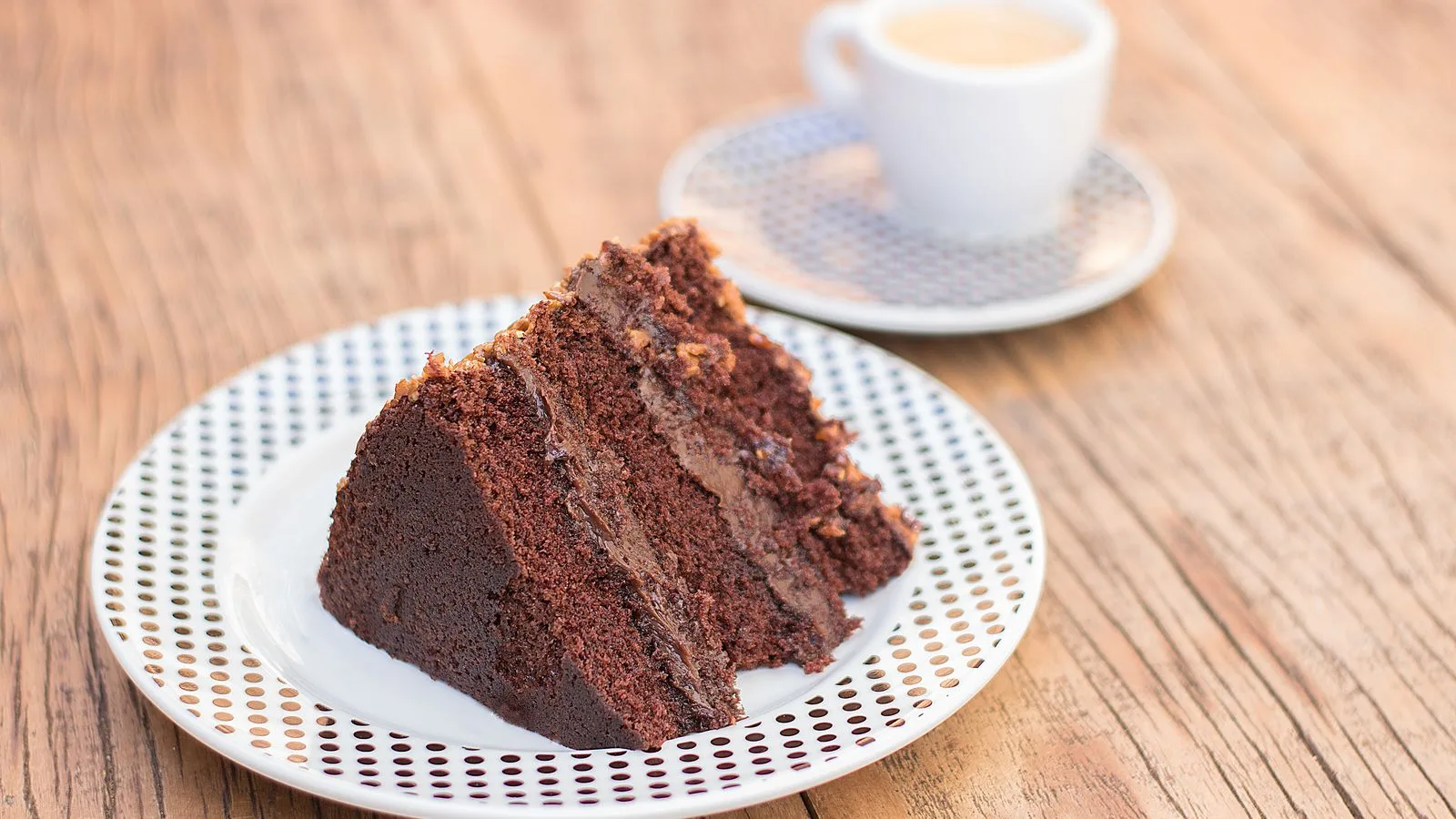 Delicious slice of chocolate cake served with coffee on a rustic wooden table, perfect for dessert lovers.