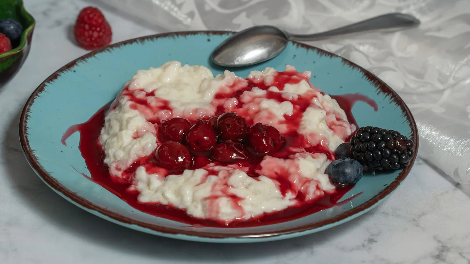 Savory rice porridge topped with sweet cherries, blackberries, and blueberries on a blue plate. Perfect breakfast or dessert.