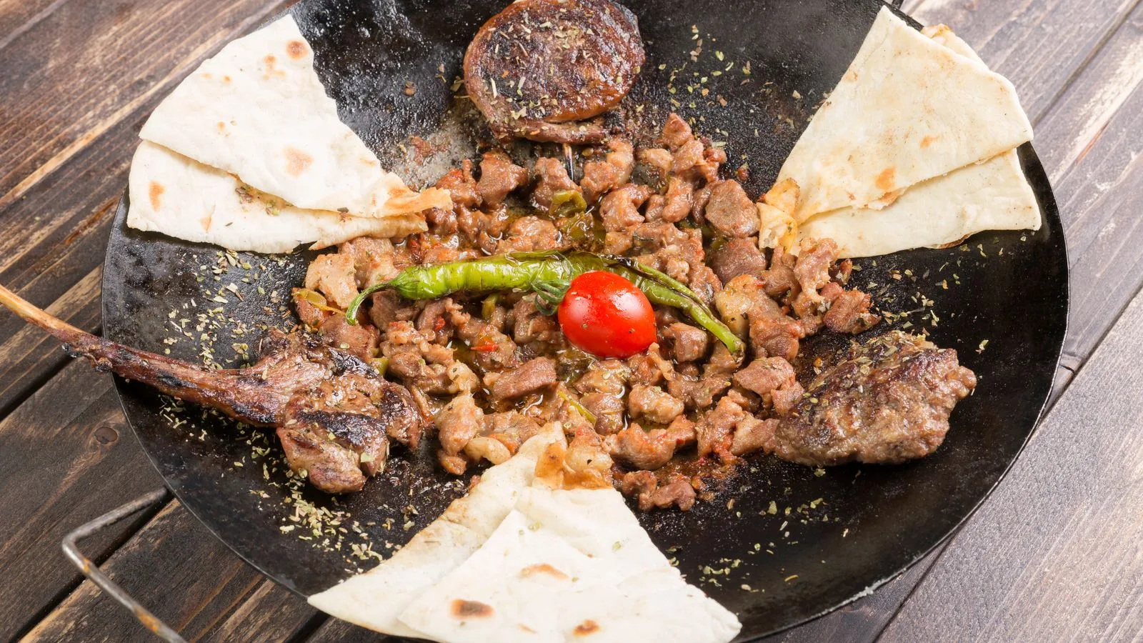 Appetizing Turkish sac tava with grilled meat, chili, and pita, served on a wooden table in Bursa.