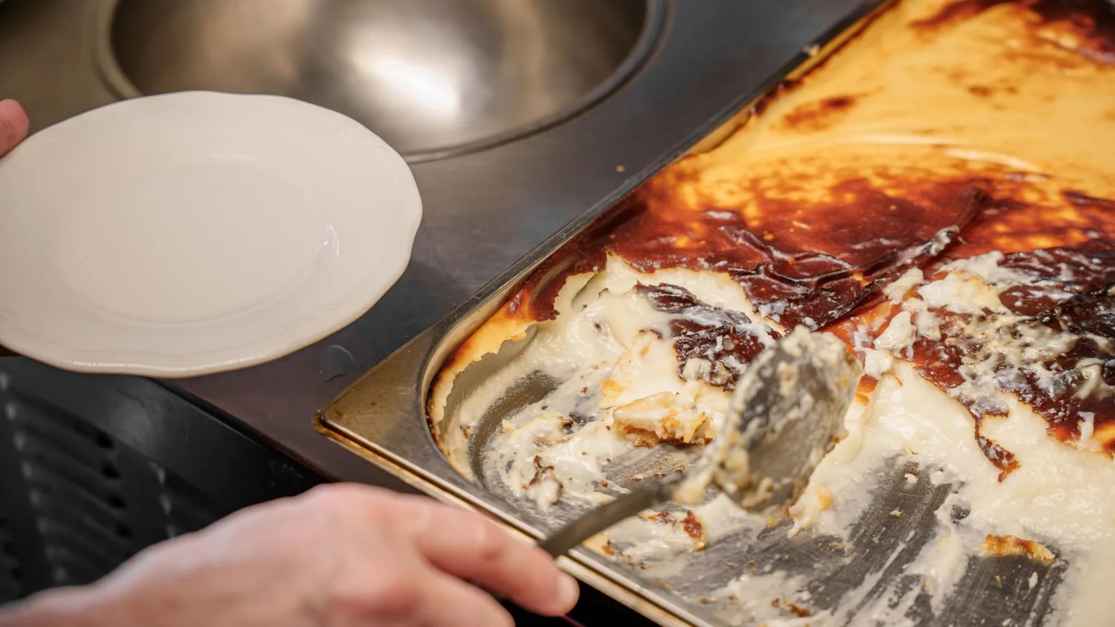 A person serving traditional Turkish rice pudding from a tray, showcasing its creamy texture.