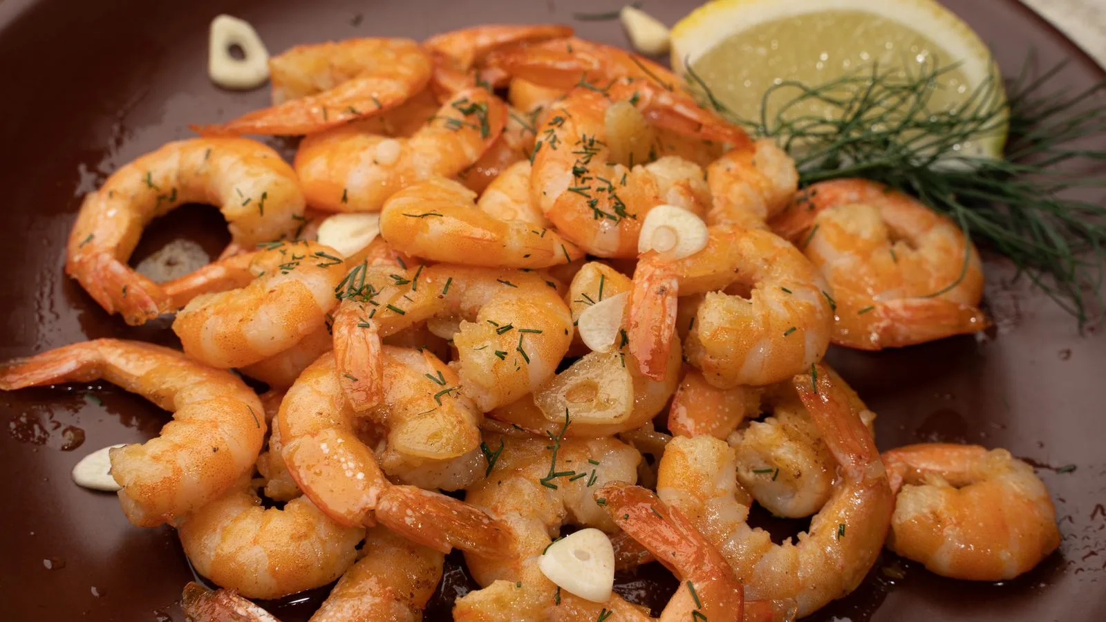 Close-up of flavorful shrimp garnished with garlic, lemon, and dill.