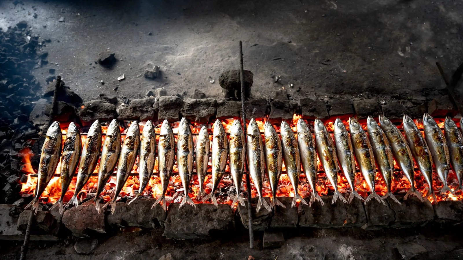 Grilled sardines cooking over a traditional charcoal fire pit. Smoky and savory.