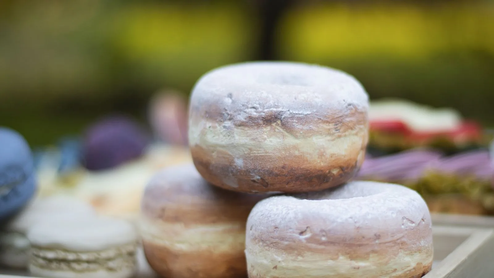 Close-up of three powdered donuts stacked on a wooden tray outdoors.