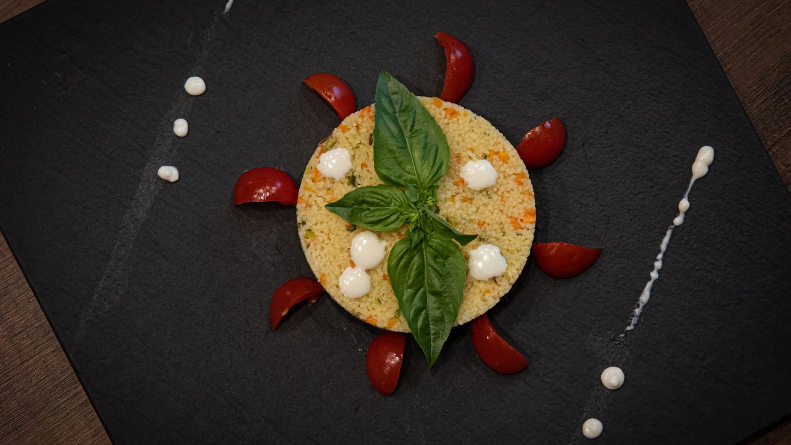 Couscous dish creatively plated with basil and cherry tomatoes on a slate plate.