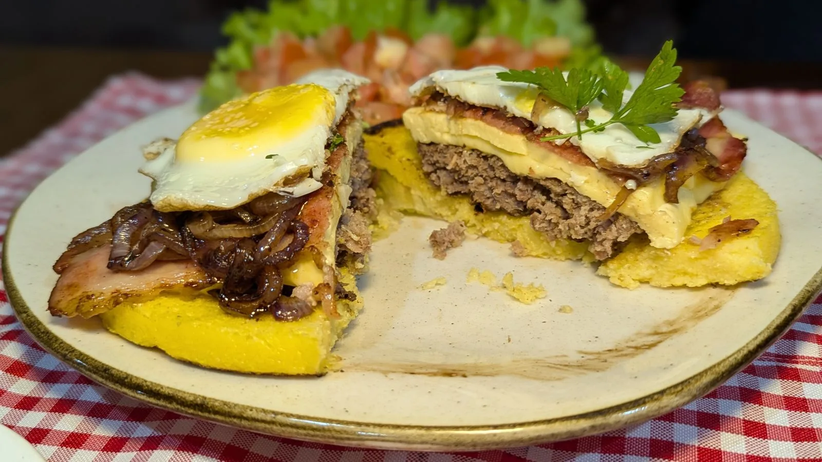 Mouthwatering Brazilian burger topped with fried egg, bacon, and cheese on a checkered tablecloth.