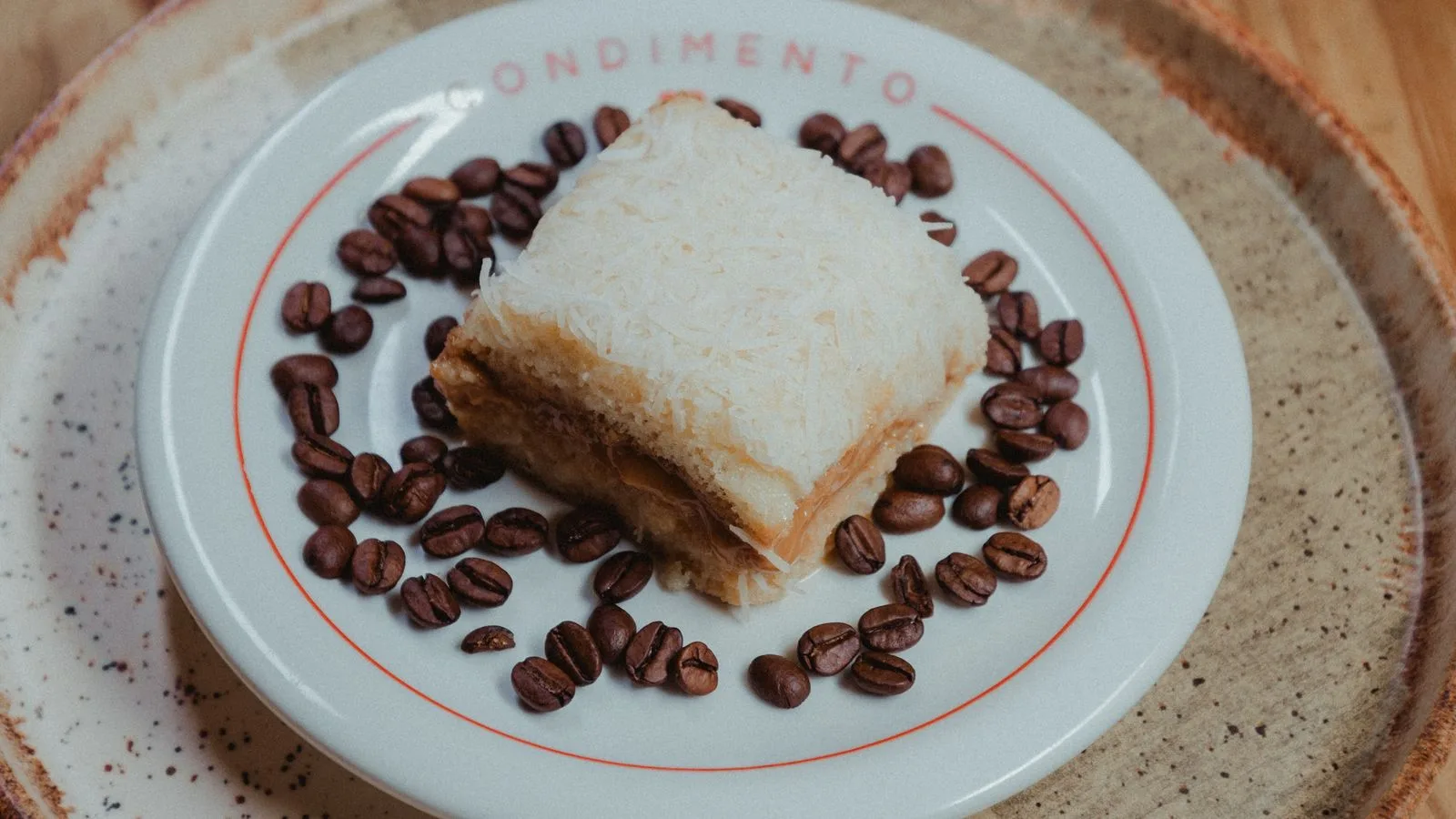 A slice of creamy coconut cake garnished with coffee beans on a rustic plate.