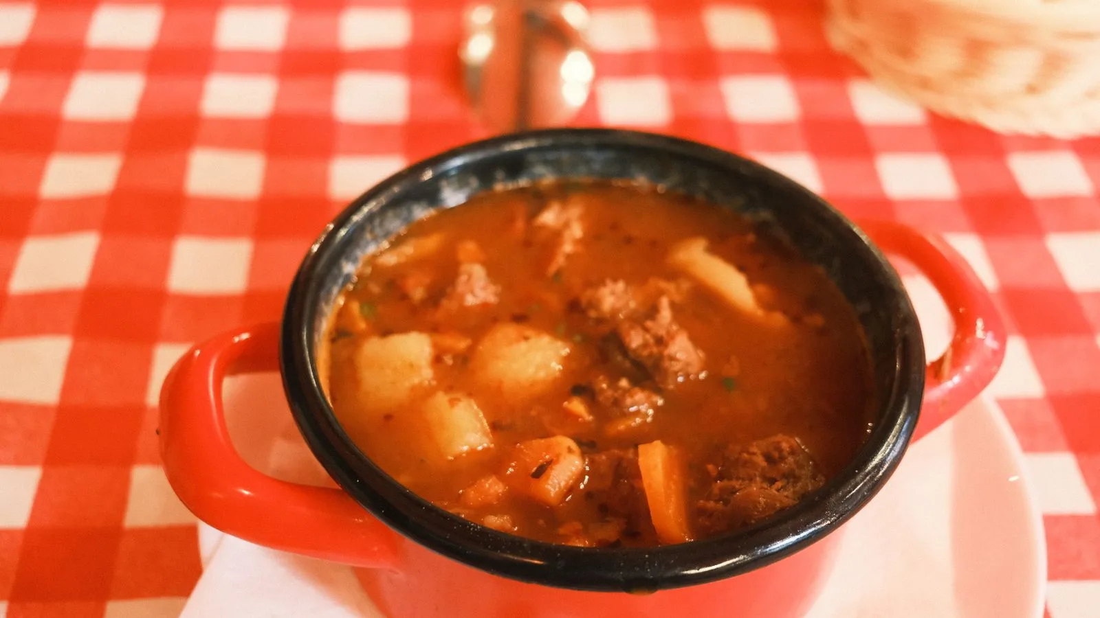 Delicious Hungarian goulash served in a red pot on a checkered tablecloth in Budapest.