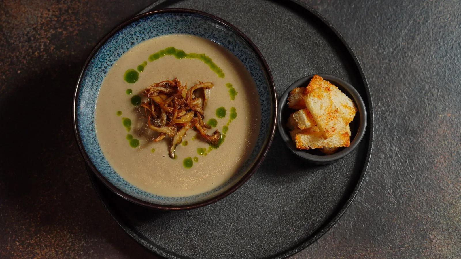 Delicious creamy mushroom soup with crispy croutons, elegantly presented on a stone background.