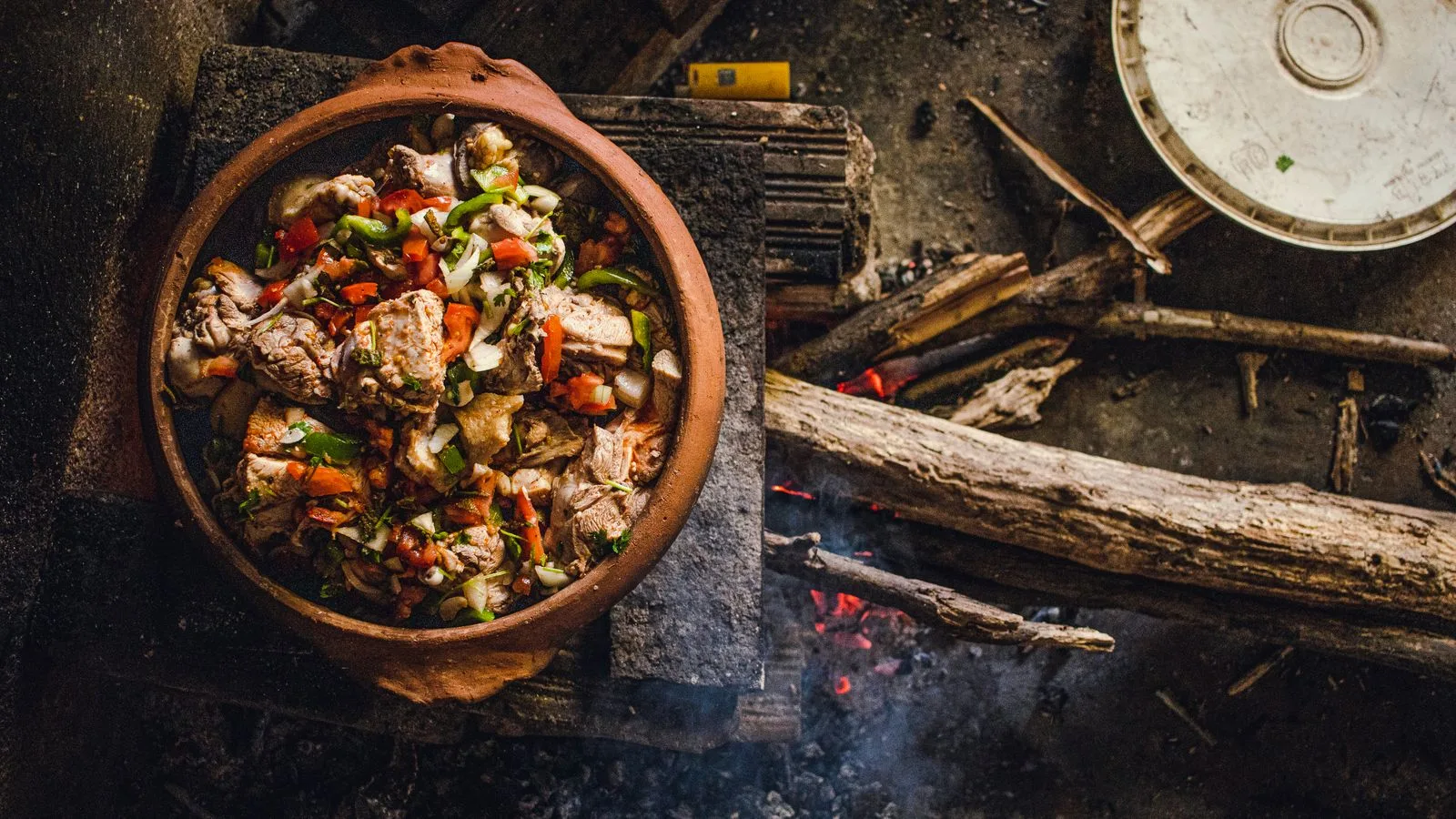 A rustic clay pot cooking meat and vegetables over an open wood fire in Brazil, showcasing traditional cuisine.