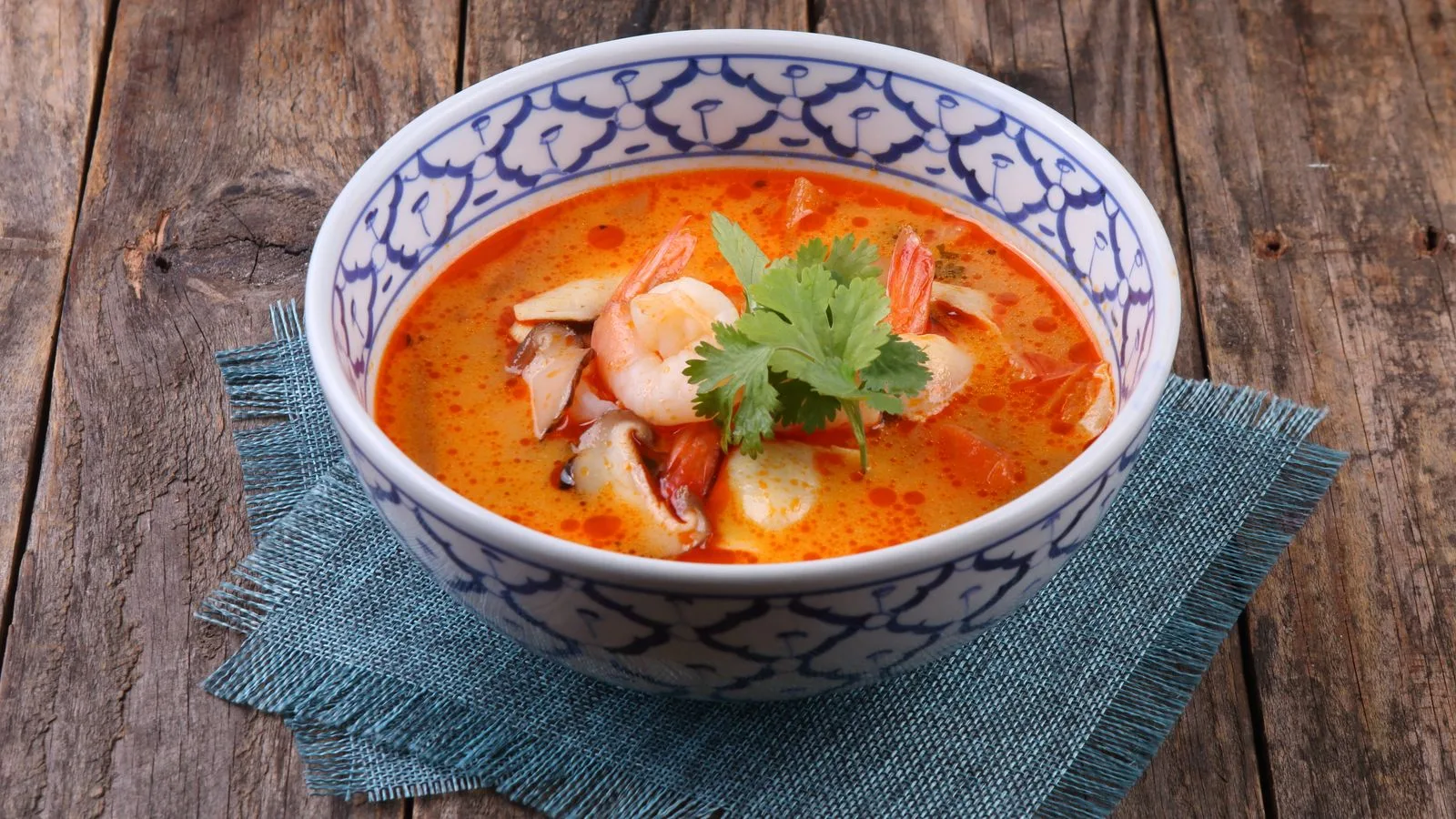 A vibrant bowl of Thai tom yum soup with shrimp and herbs served on rustic wood.