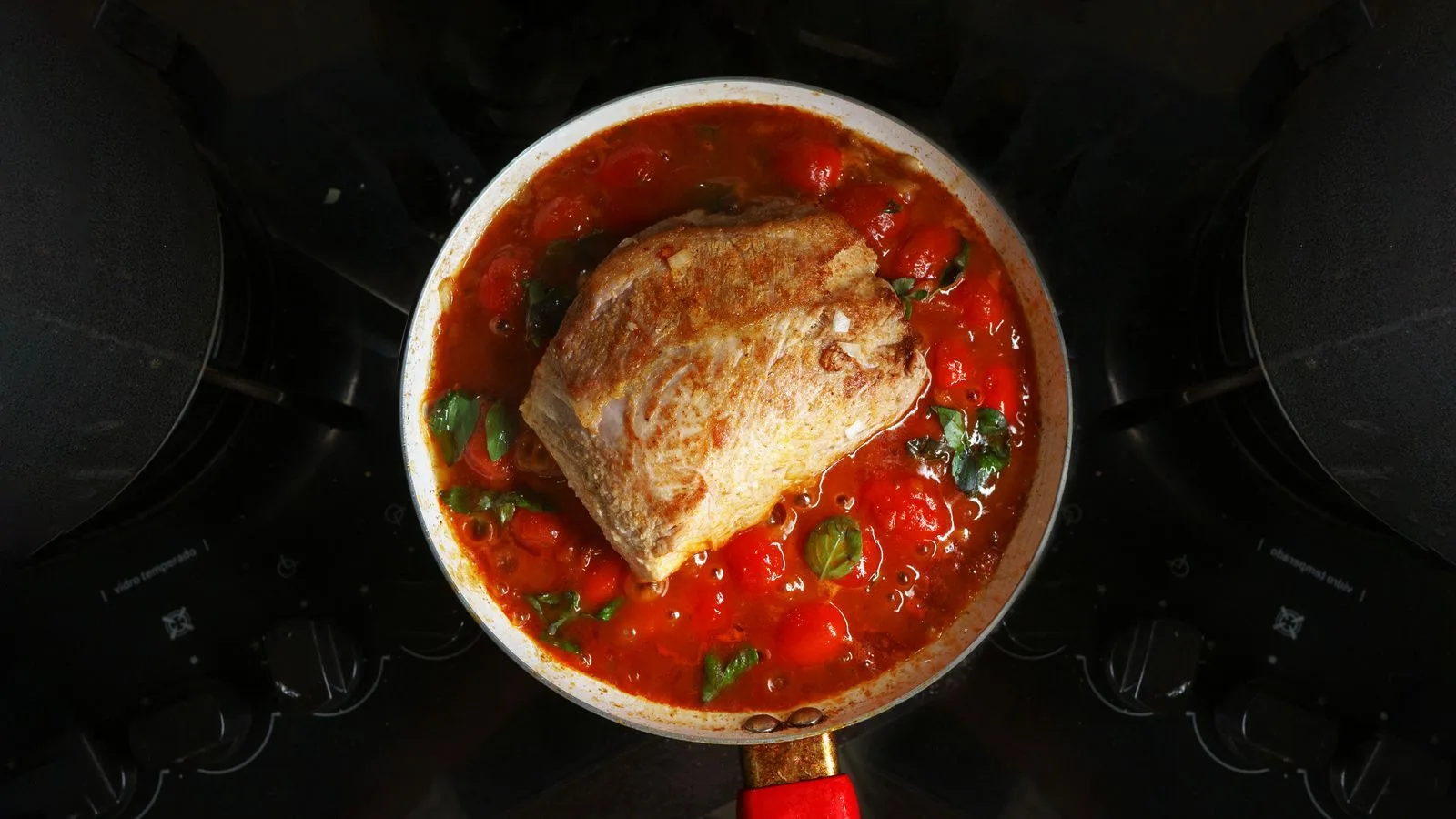 A savory roast beef cooked in rich tomato sauce with herbs, atop a stovetop.