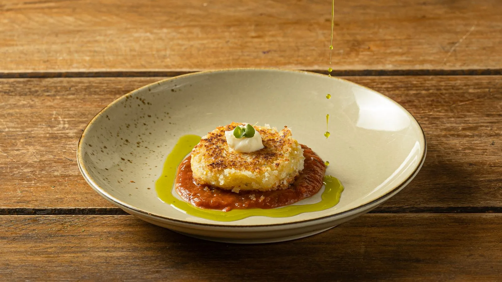 Mouthwatering risotto cake topped with cream and drizzled olive oil on a wooden table.