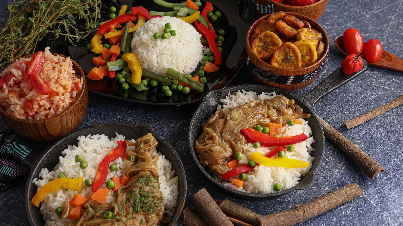 A vibrant display of traditional rice dishes with vegetables, plantains, and chicken in iron pans.