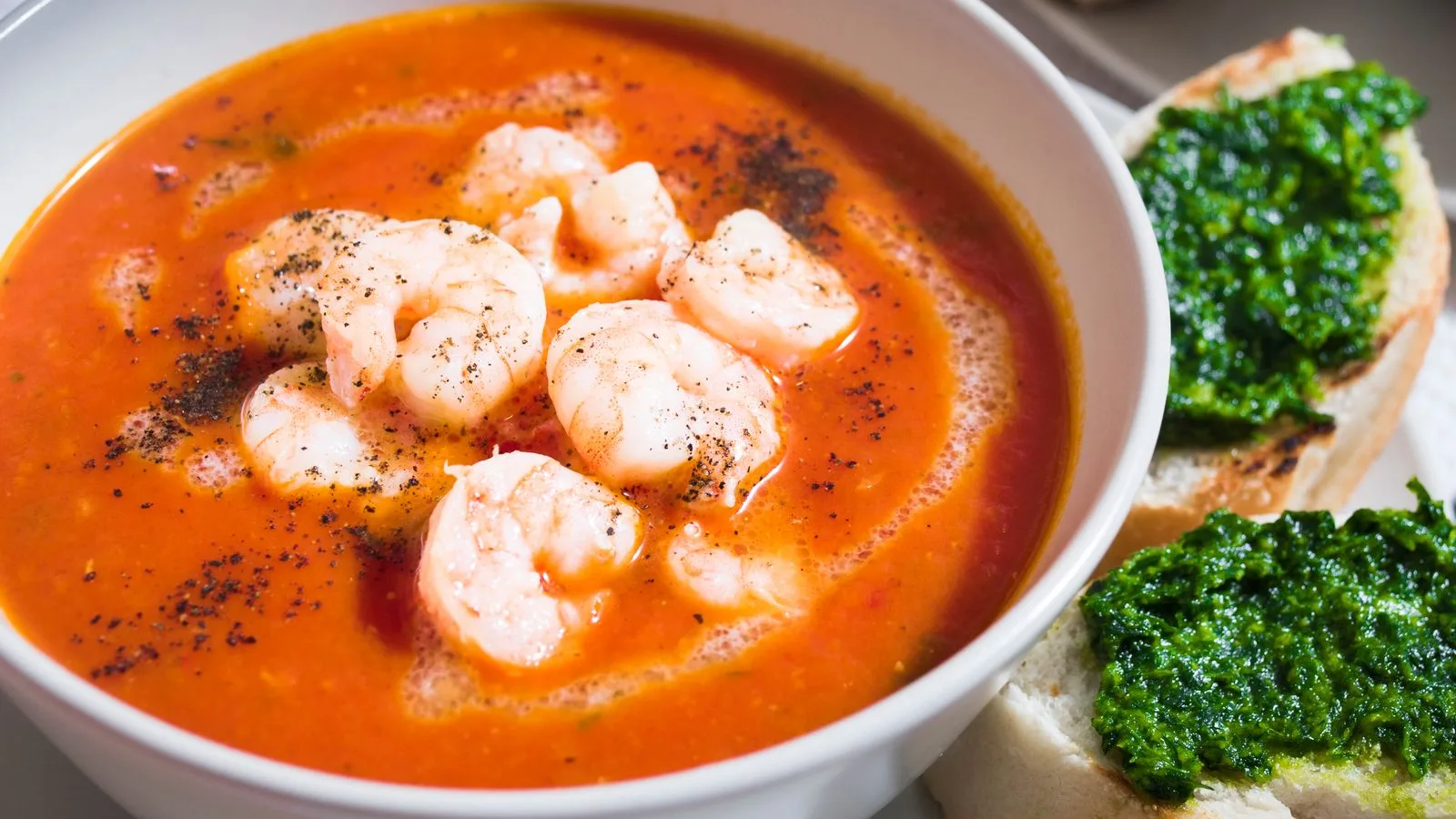 Delicious shrimp soup served with garlic bread topped with fresh pesto, perfect for a hearty meal.