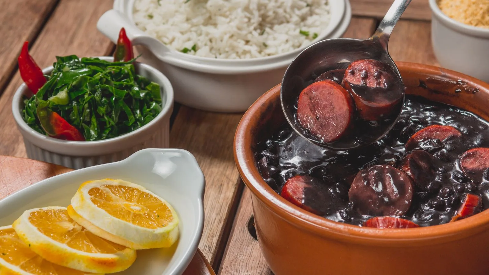 Delicious Brazilian feijoada with rice, greens, and orange slices served on a wooden table.