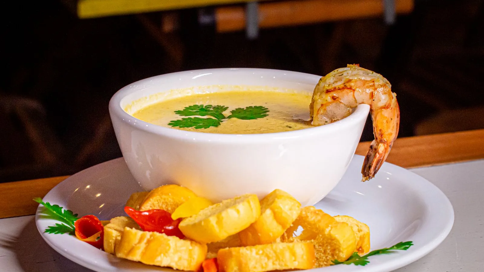 A bowl of creamy shrimp soup garnished with cilantro and served with bread slices on a plate.