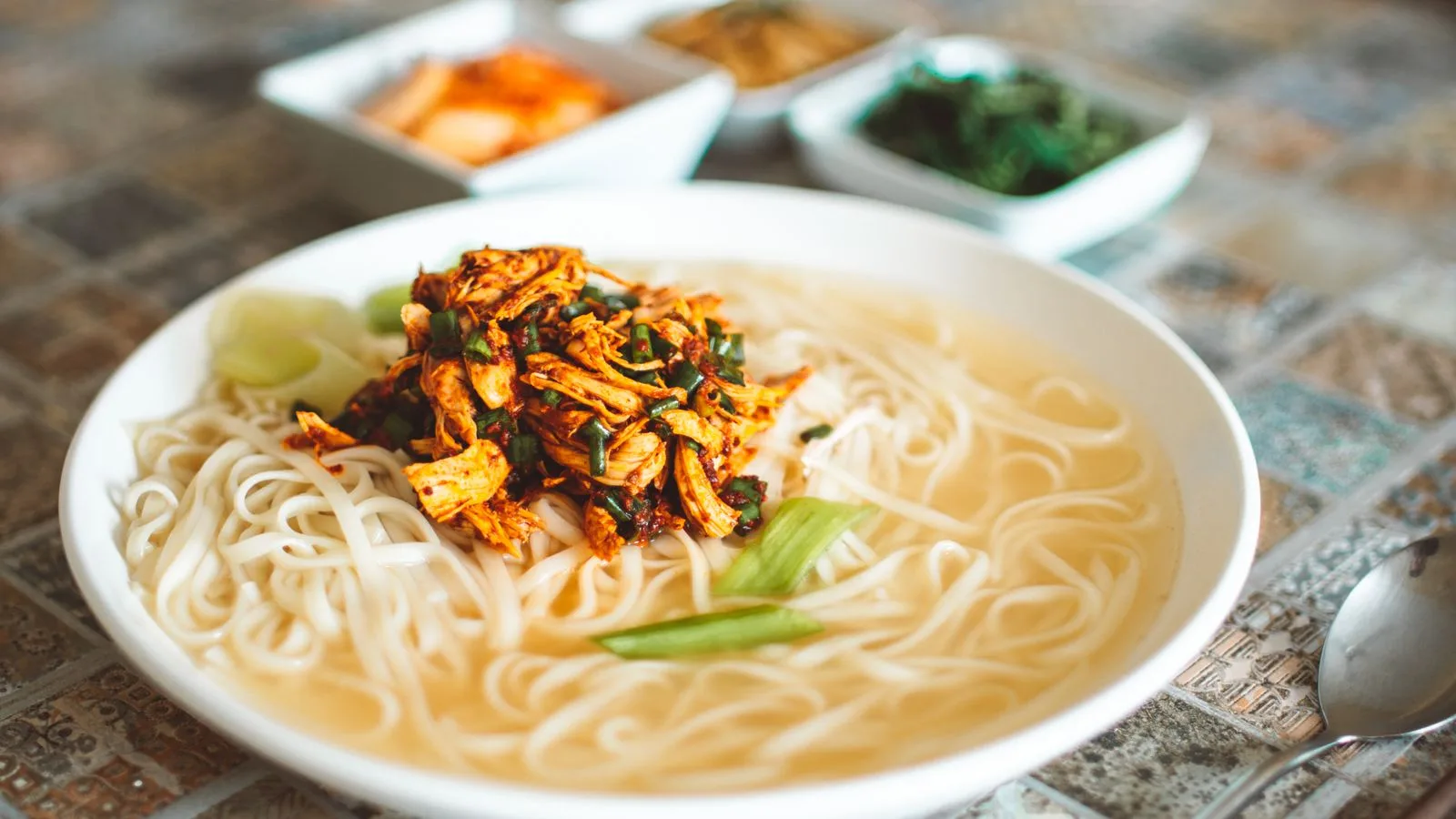 Delicious spicy chicken noodle soup served with lime and spices in a ceramic bowl.