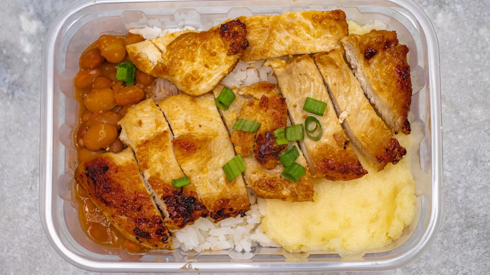 Top view of a tasty home-cooked meal with grilled chicken, beans, and rice in a bento box.