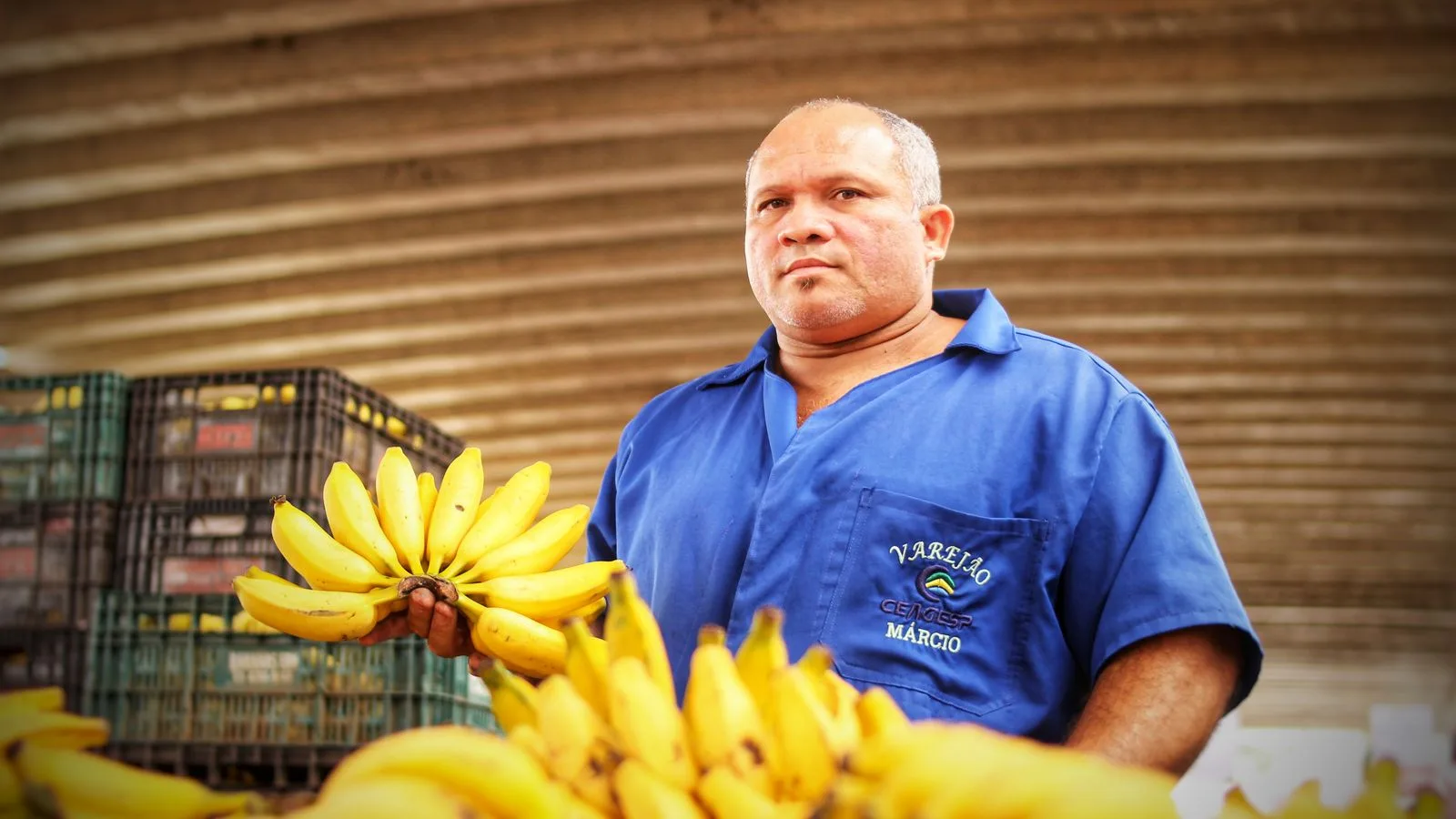 A fruit vendor in São Paulo holding a bunch of bananas in a busy market setting.