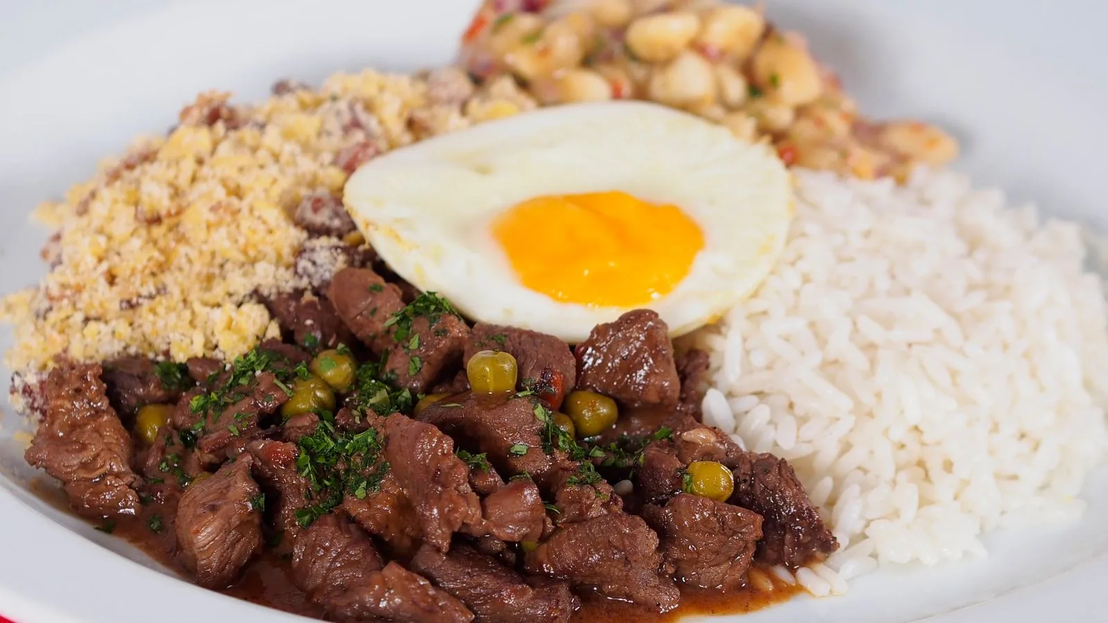 A plate of Brazilian feijoada with rice, beans, farofa, and a fried egg.