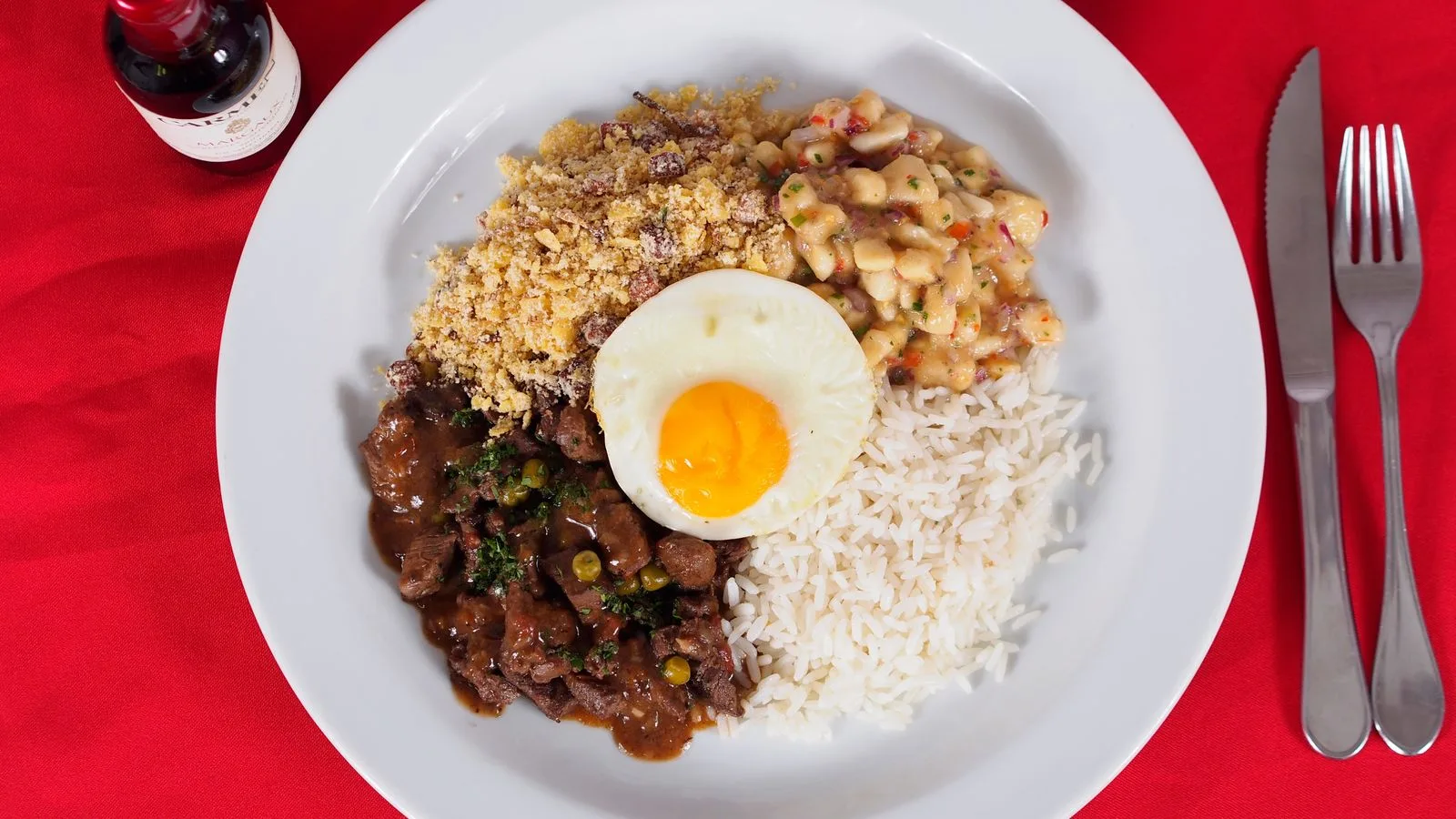 A vibrant Brazilian Feijoada meal with rice, beans, and a fried egg on a red background.