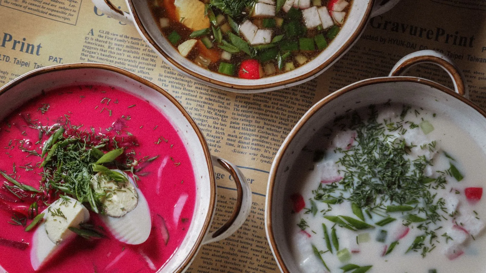 Top view of three colorful soups in rustic bowls on vintage newspaper.