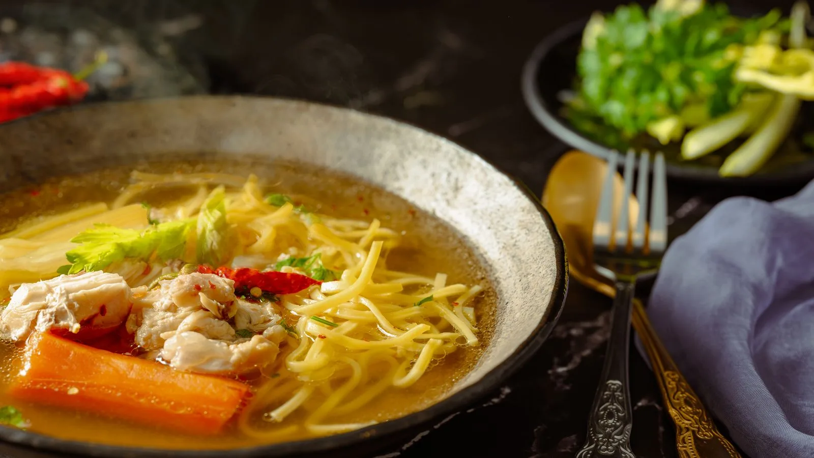 Capture of a flavorful chicken noodle soup with garnishes in a rustic setting.