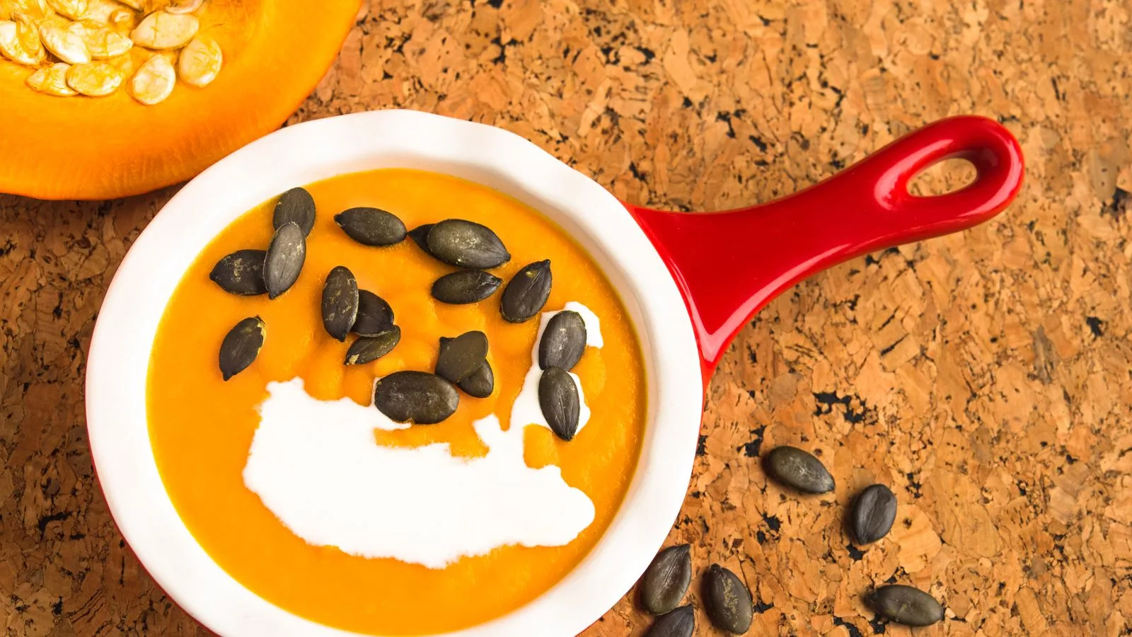 Appetizing close-up of pumpkin soup with cream and seeds in a red bowl.