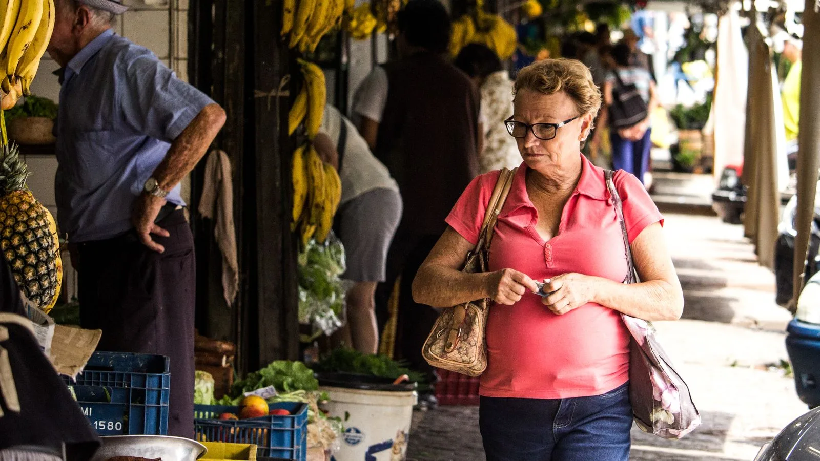 A lively urban street market scene with people shopping for fresh produce like bananas and pineapples.