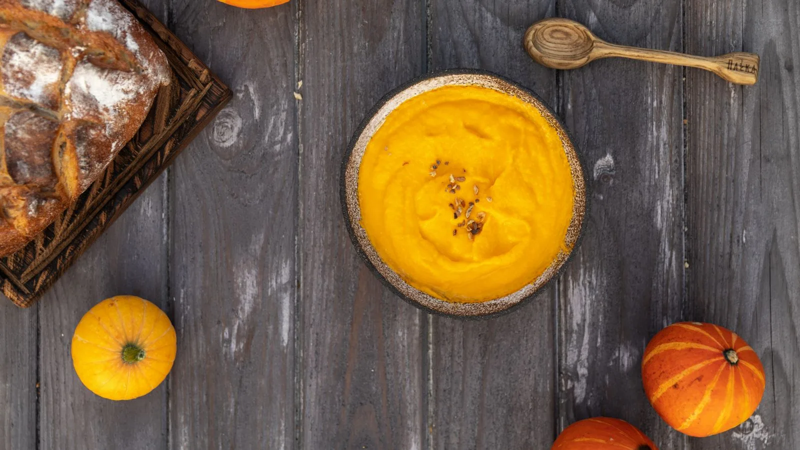 Top view of creamy pumpkin soup, artisan bread, and pumpkins on rustic wooden surface, ideal for autumn food themes.