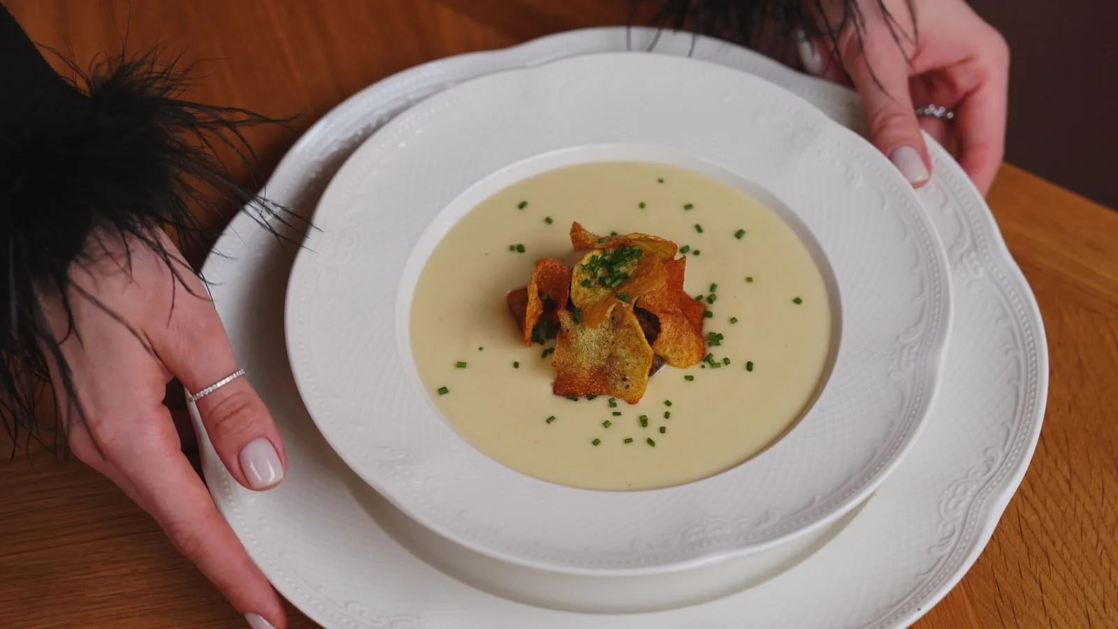 A gourmet creamy soup garnished with crispy toppings is beautifully served on white porcelain.