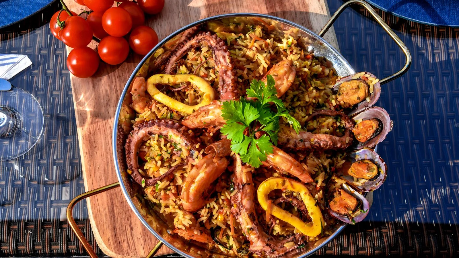 A vibrant seafood paella featuring octopus, shrimp, mussels, and fresh vegetables served outdoors.