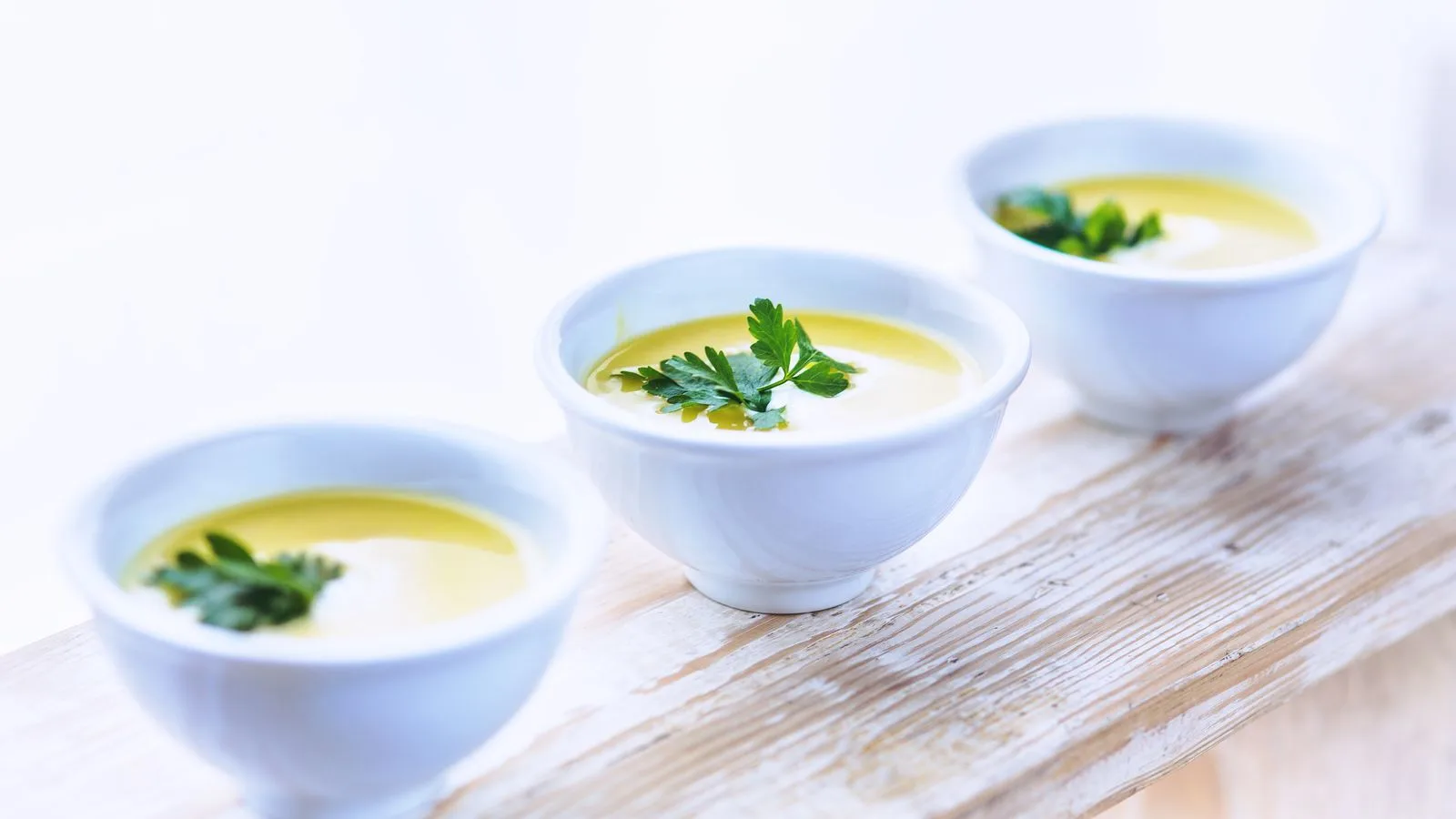 Three bowls of creamy parsnip soup garnished with fresh parsley on a rustic wooden surface.