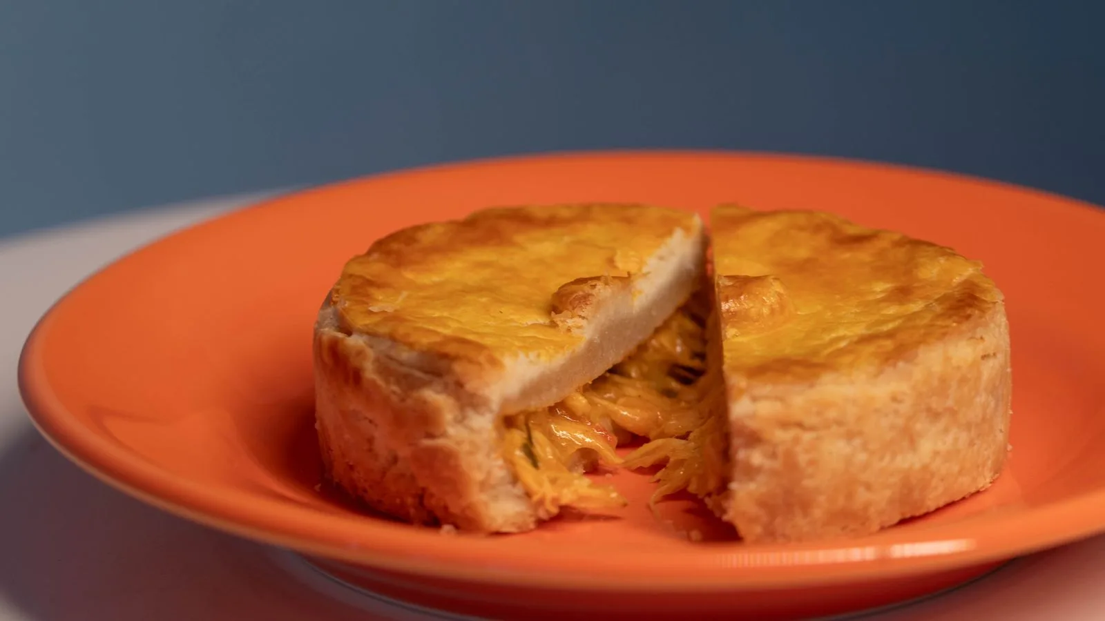 Close-up of a homemade chicken pie sliced open on an orange plate with warm lighting.