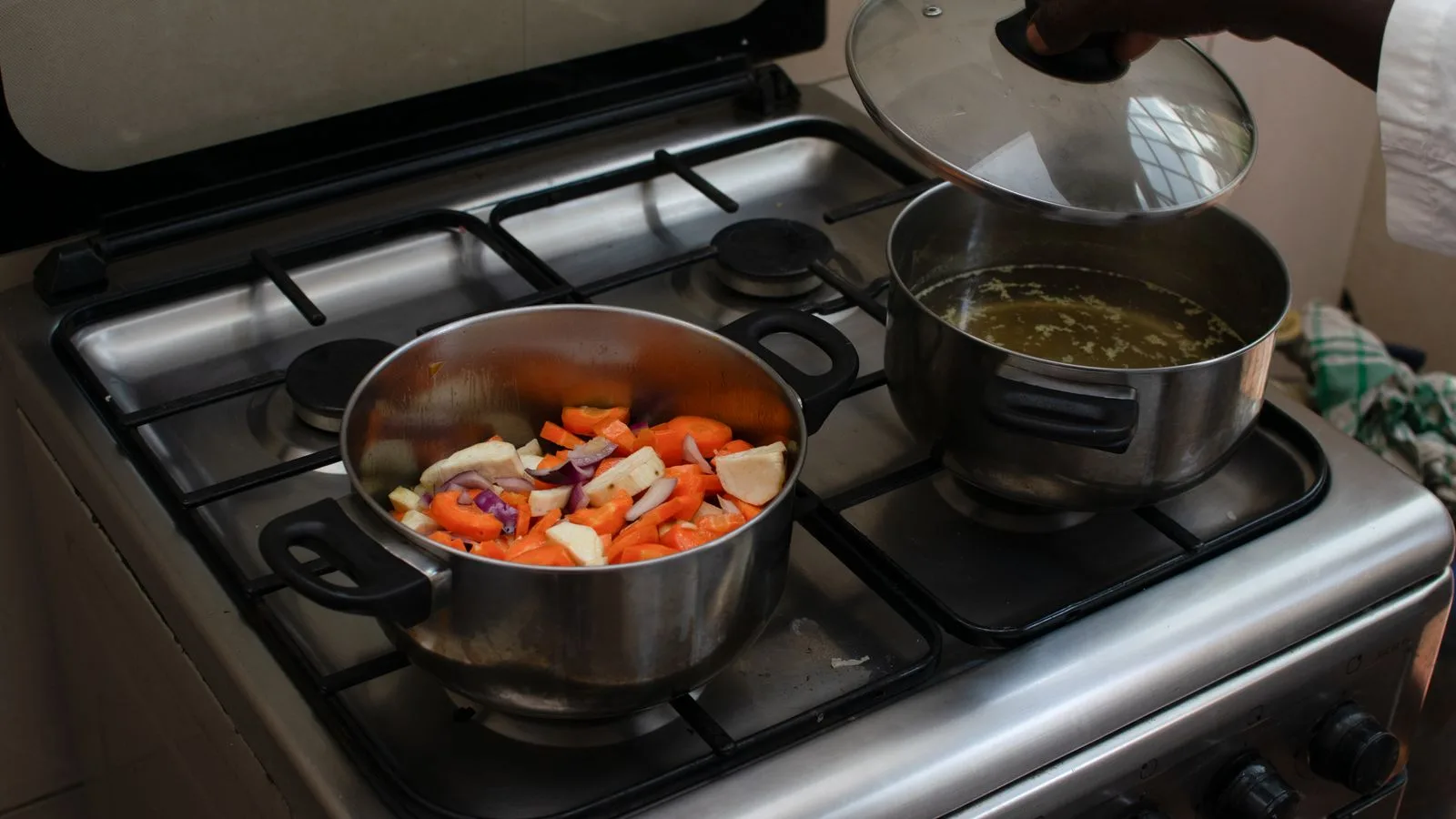 A kitchen scene featuring fresh vegetables being cooked in pots on a gas stove.