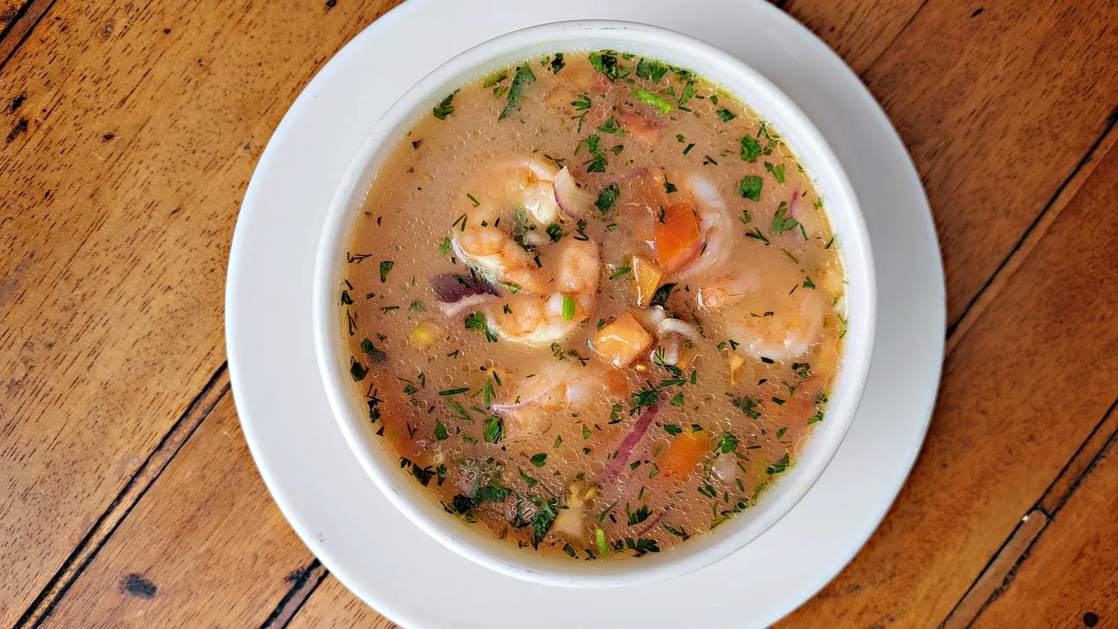 Appetizing shrimp stew with vegetables in a white bowl on a wooden table, showcasing Ecuadorian flavors.