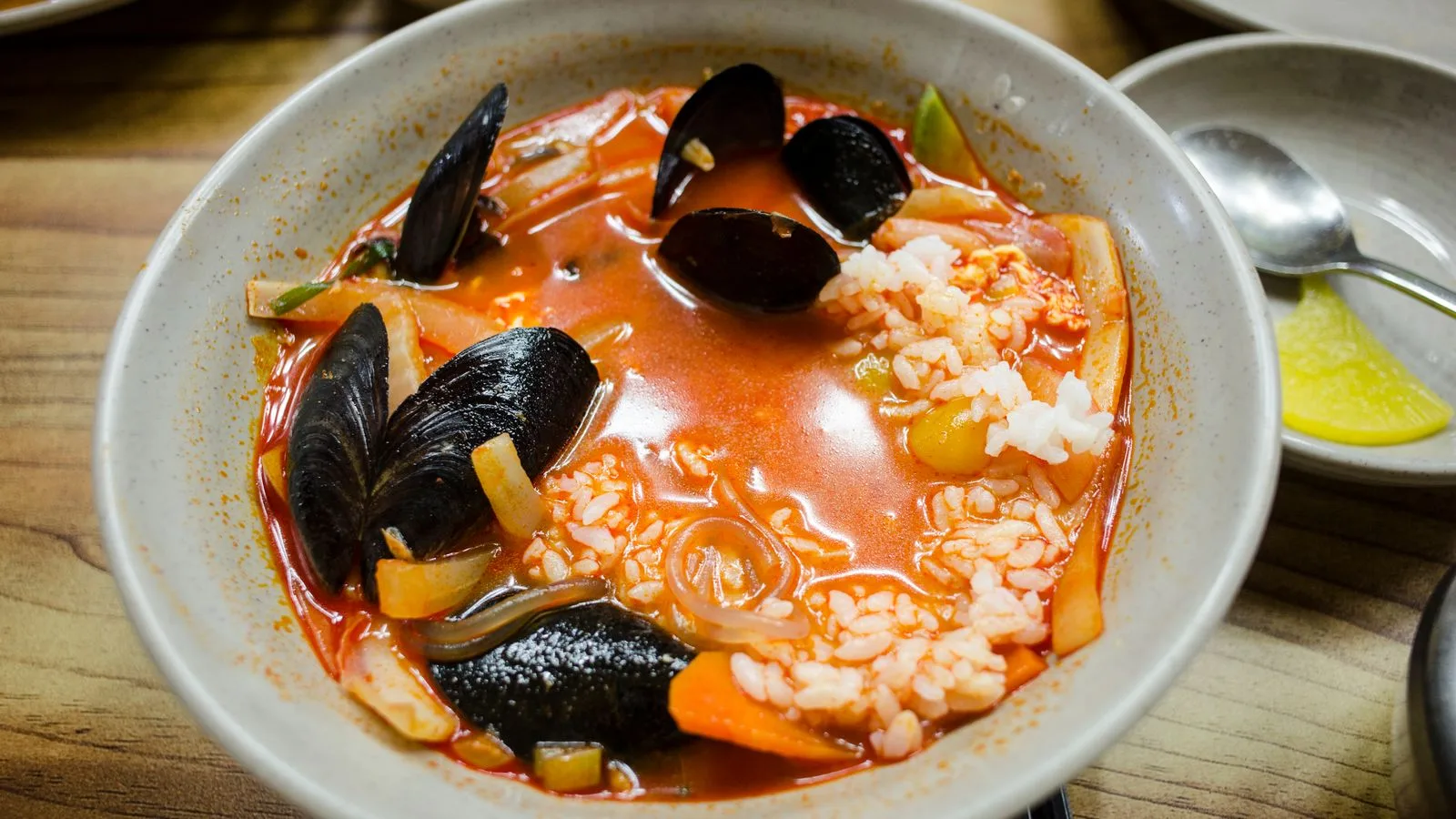 Delicious bowl of spicy seafood soup with fresh mussels, rice, and vegetables in a vibrant broth.