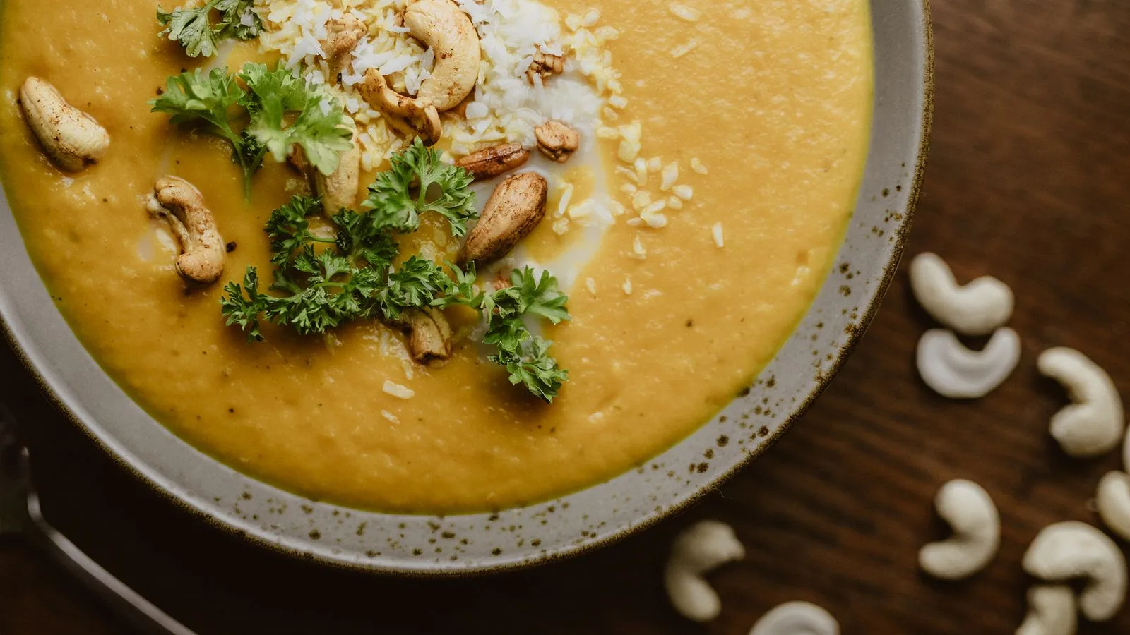 Delicious creamy pumpkin soup garnished with cashews and fresh herbs in a bowl.
