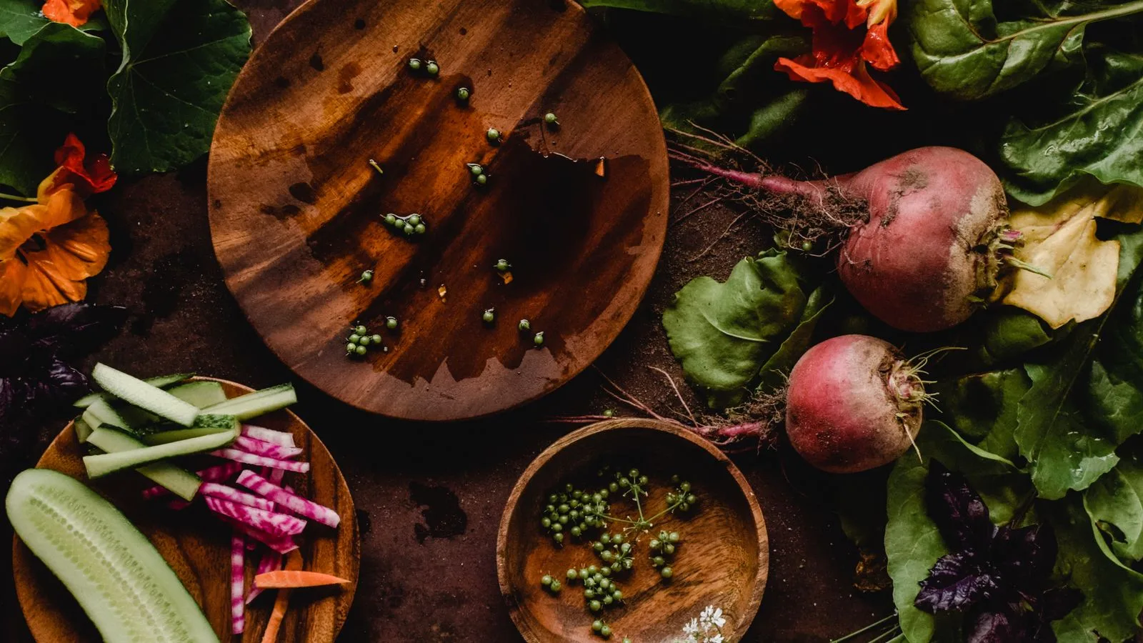 A rustic flatlay showing fresh organic vegetables including beets, cucumbers, and peas.