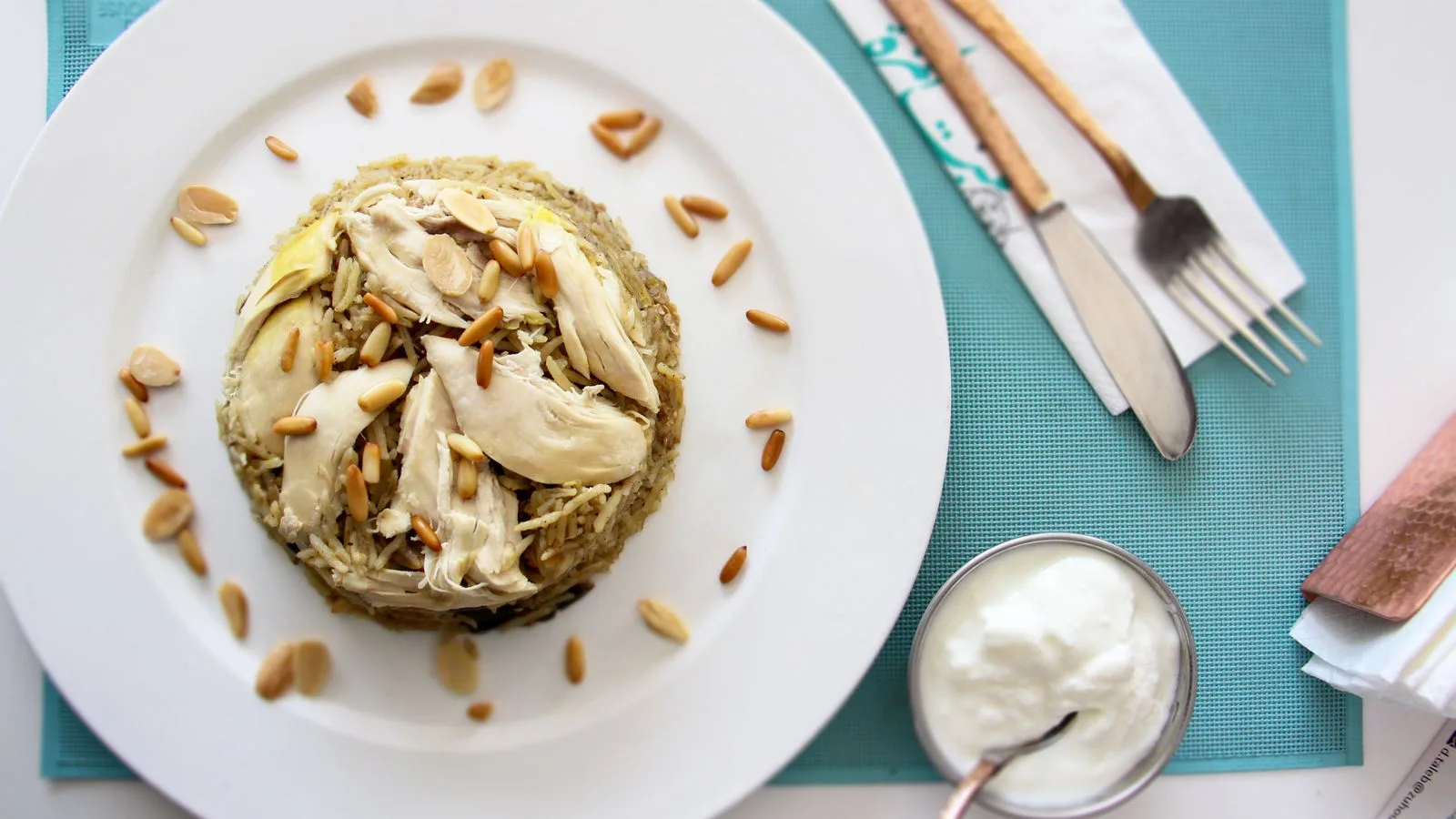 Delicious Middle Eastern chicken and rice dish garnished with pine nuts and almonds, served with creamy yogurt.